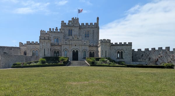 Château d'Hardelot de face. Au premier plan, une grande pelouse qui donne sur une montée de marches. Le château est composé de plusieurs tours.