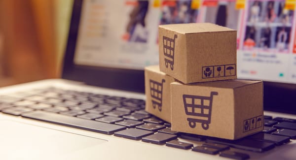 clavier d'ordinateur portable sur lequel se trouve trois cartons empilés avec un le logo d'un chariot représentant la vente en ligne.